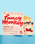 Fancy Monkey Vanilla Instant Pudding & Dessert Mix box shown next to a layered vanilla pudding dessert in a glass jar with berries and a biscuit, on a light blue background.