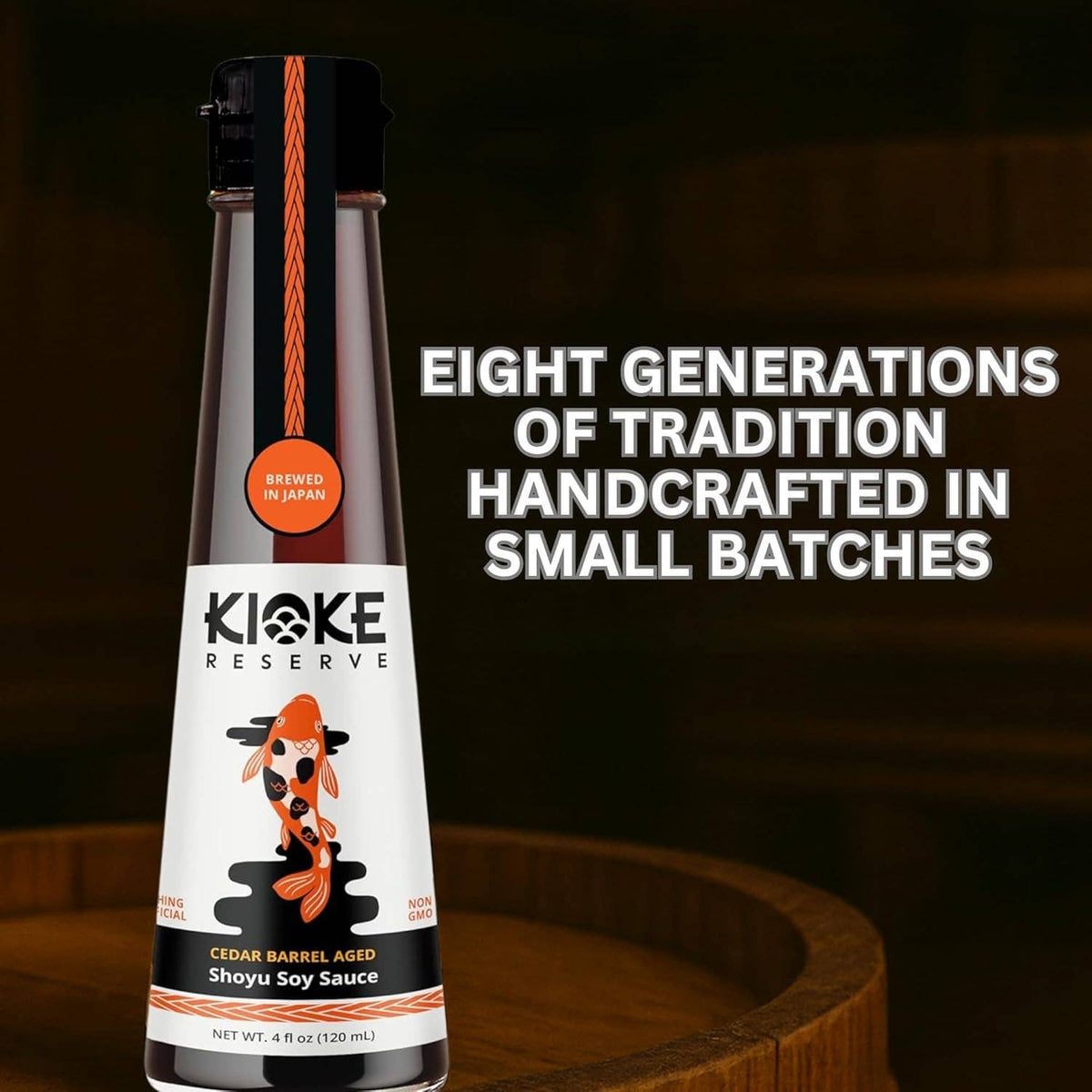 A bottle of Kioke Reserve Cedar Barrel Aged Shoyu Soy Sauce stands on a wooden barrel surface against a dark wood background. The bottle has a black cap, a white label with a koi fish illustration, and orange accents.