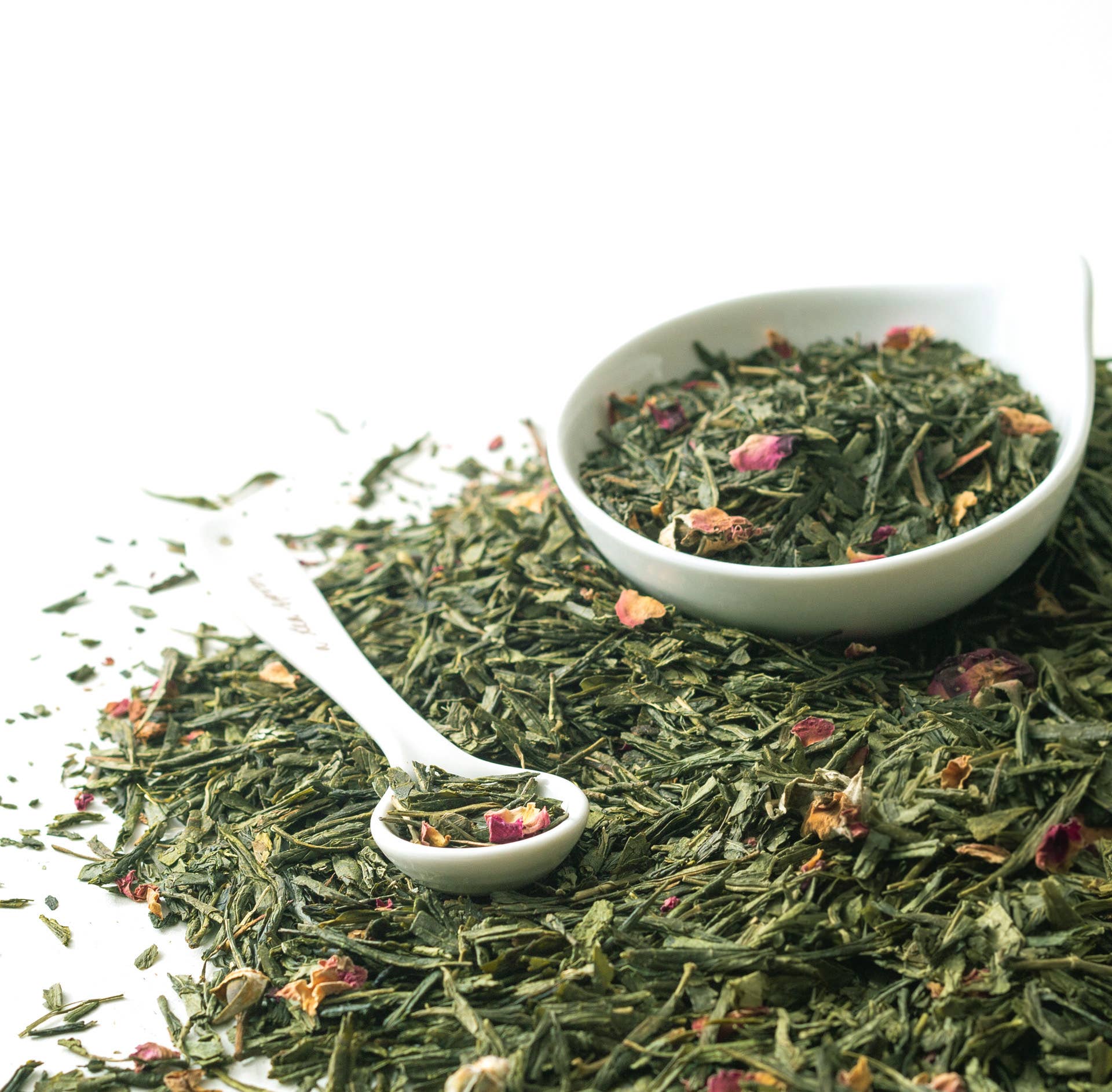 White bowl and spoon filled with green tea leaves on a white background
