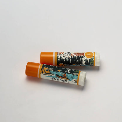 Two lip balm tubes with outdoor-themed packaging on a light gray background