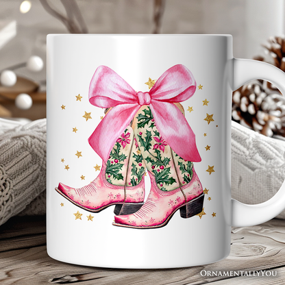 White mug with pink cowboy boots and a bow design on a wooden surface.