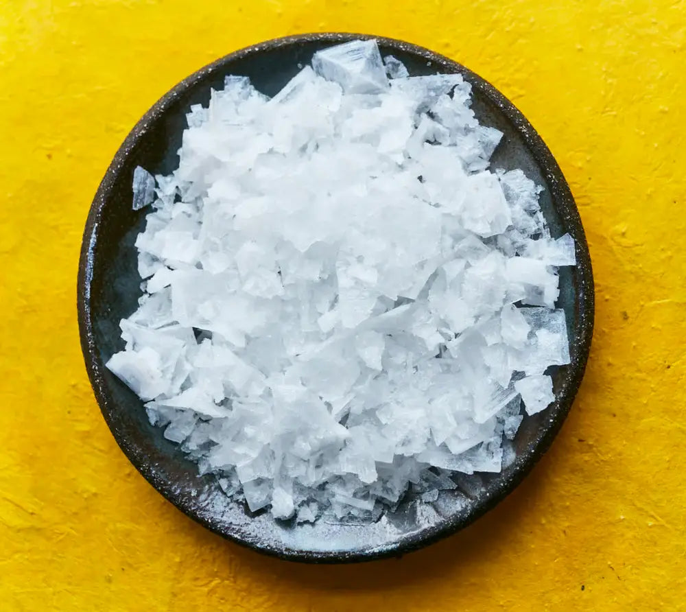Coarse salt in a black bowl on a yellow background