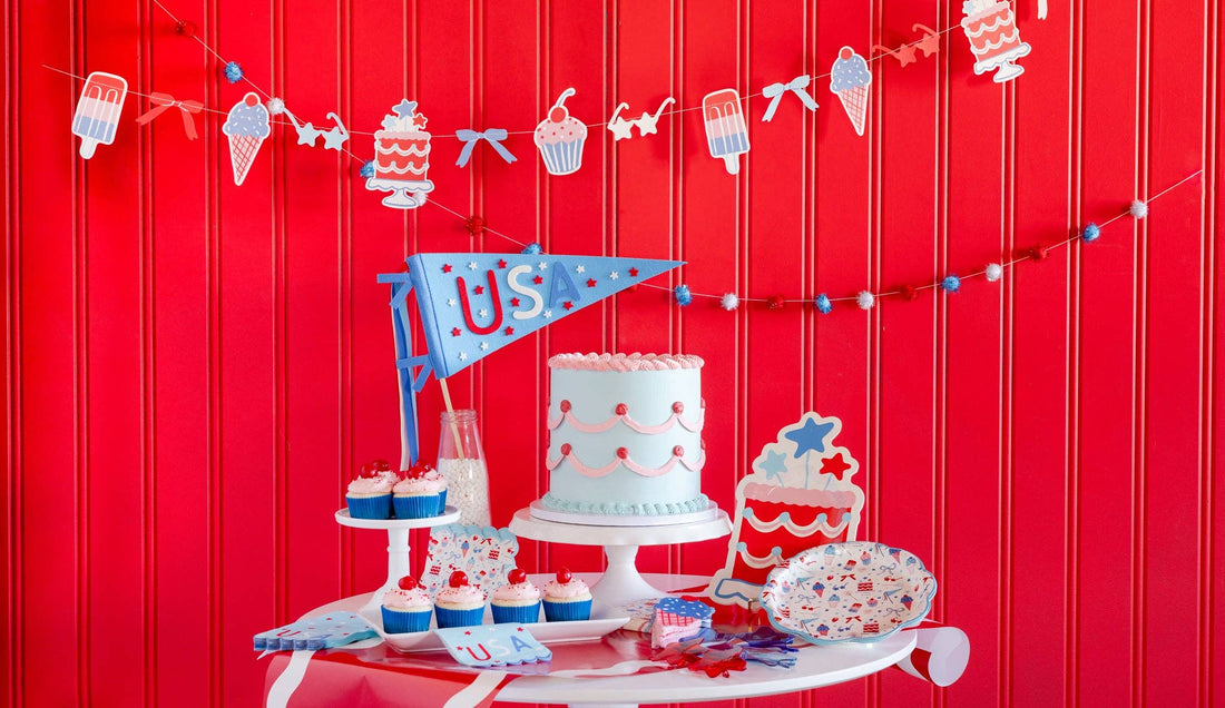 Decorative setup with a cake, cupcakes, and party decorations against a red background.