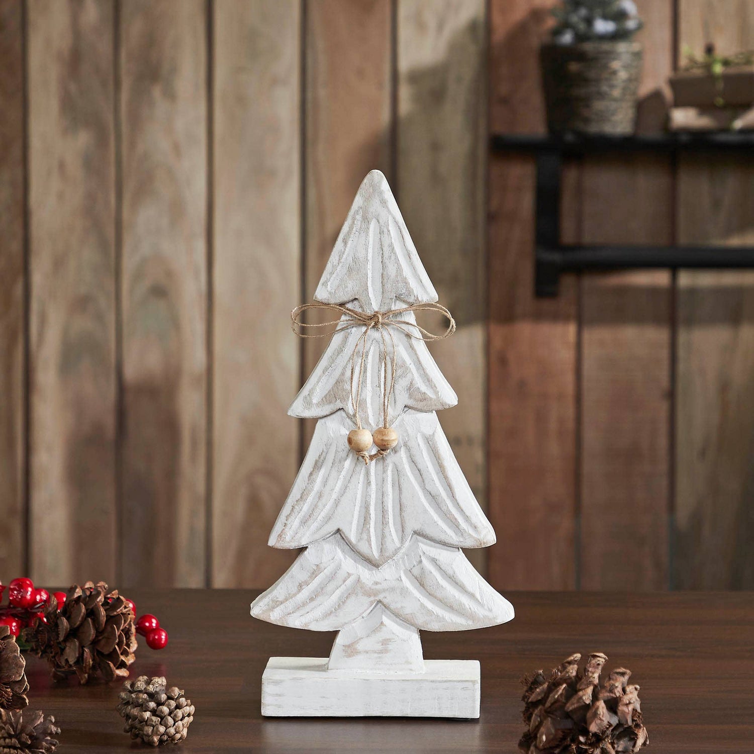 Decorative white Christmas tree with a bow on a wooden surface with pinecones and berries.
