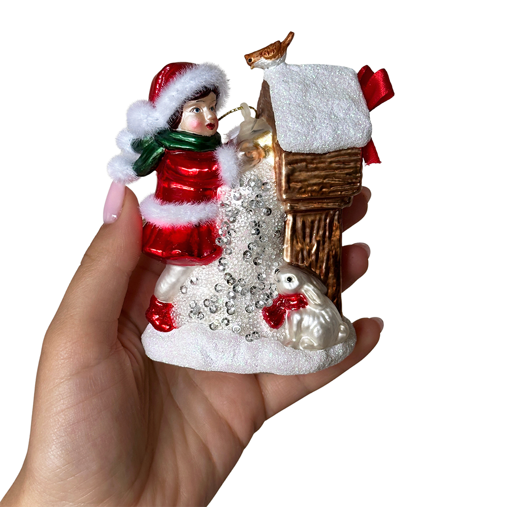 Hand holding a Christmas-themed ornament with a person, birdhouse, and birds.