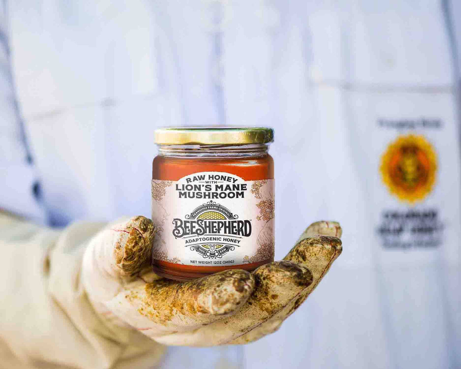 Jar of raw honey with a label held by a hand, against a blurred background.