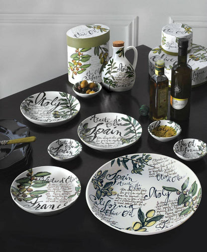 Table setting with ceramic plates, bottles, and jars featuring olive designs and text on a dark surface.