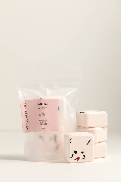 Packaged shower steamers with a pink label on a light gray background