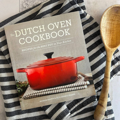 Dutch oven cookbook with a red pot on the cover, placed on a black and white striped towel.