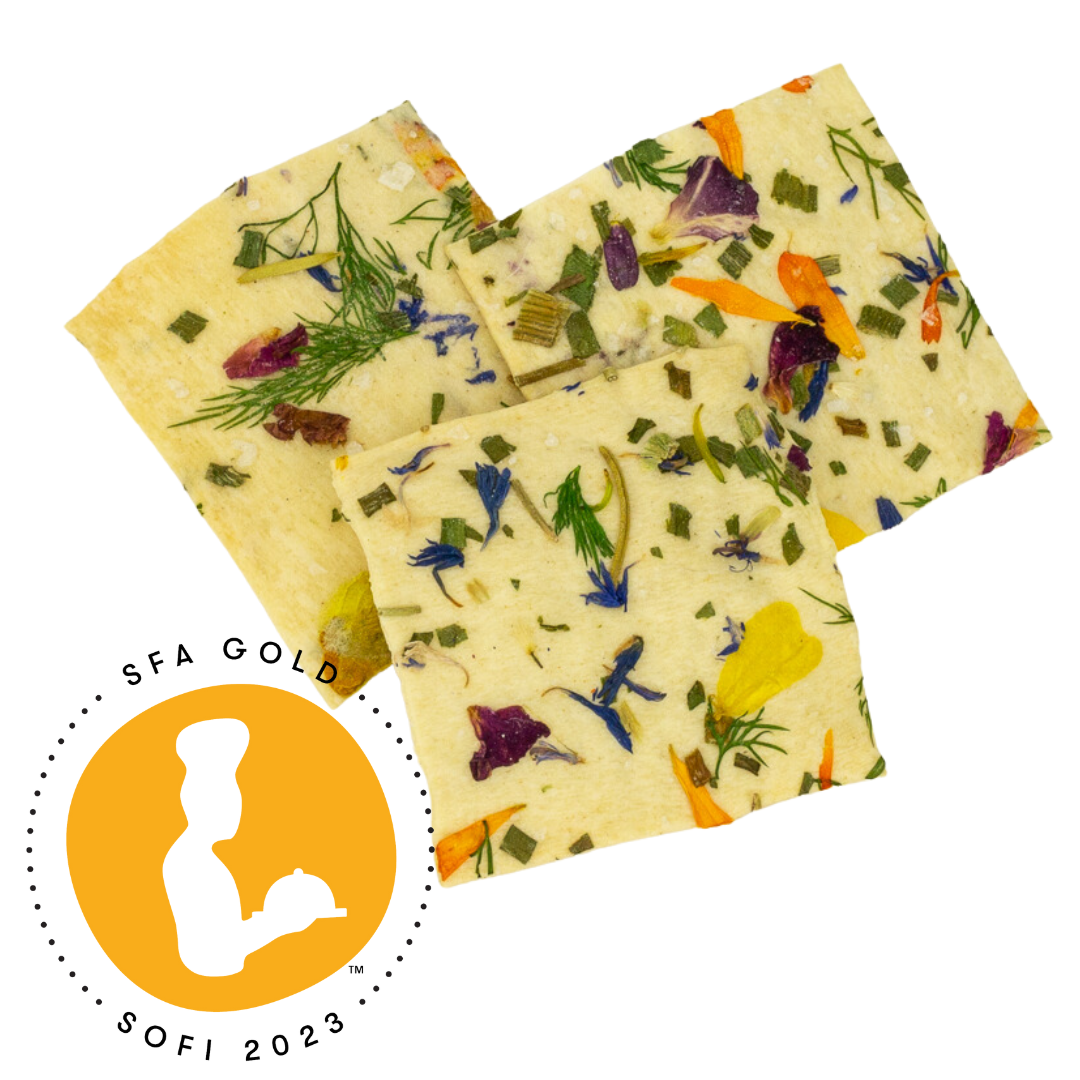 Three square crackers with floral and herb toppings on a white background, featuring an SFA Gold award logo.