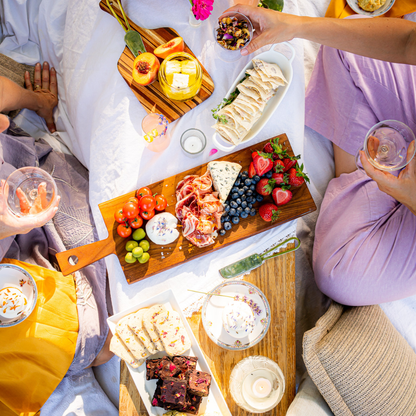 People enjoying a picnic with charcuterie board and drinks on a blanket.