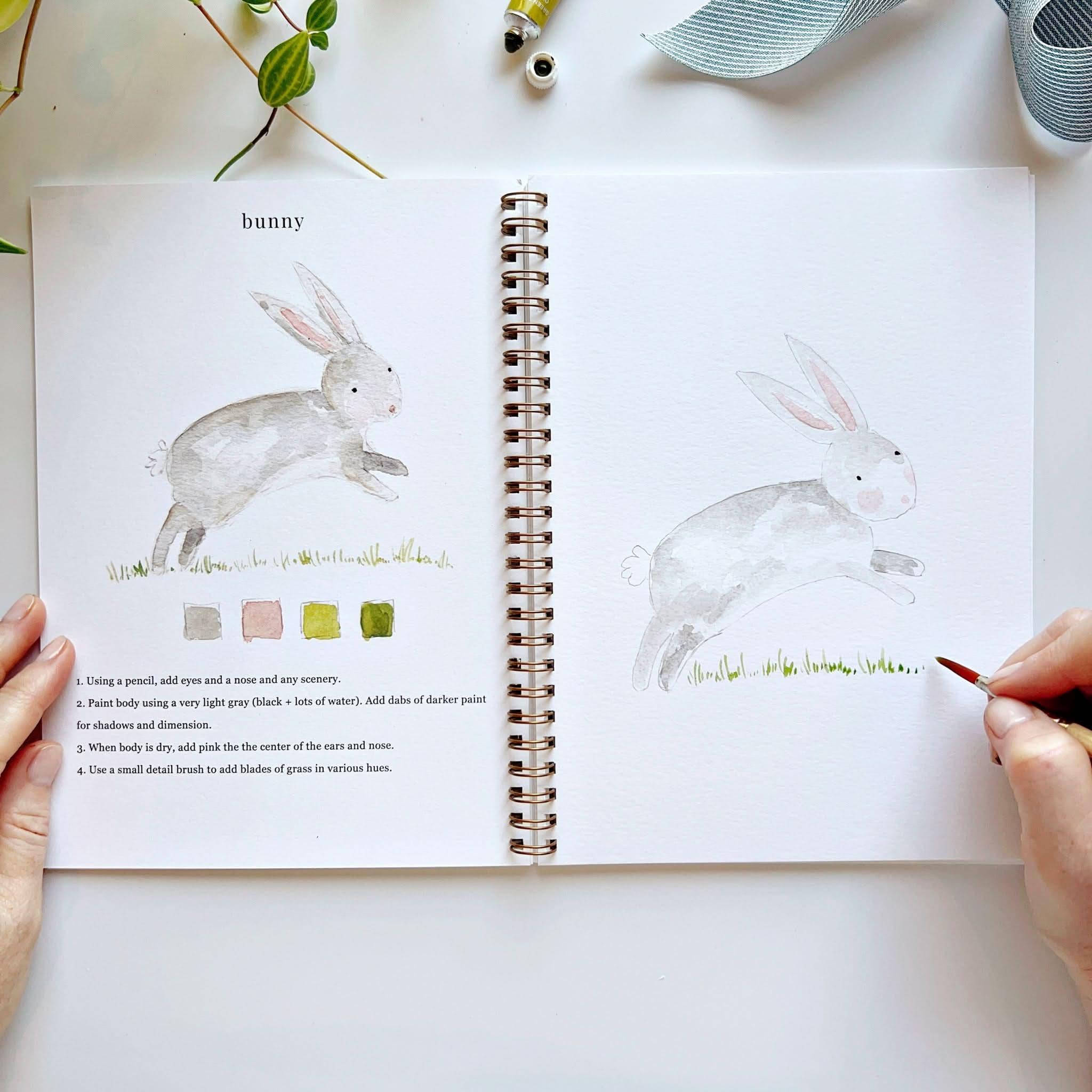 Open book with rabbit illustrations and painting instructions on a white surface.