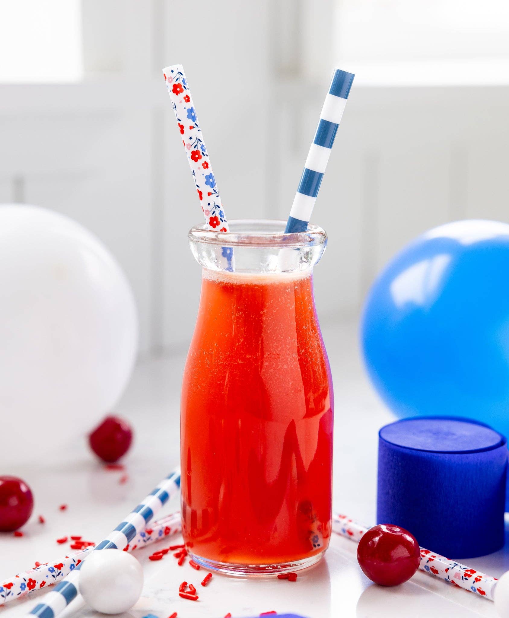 Glass of red juice with two straws and blue balloons on a white background
