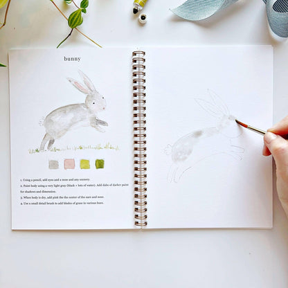 Open notebook with drawing of a rabbit and a hand holding a paintbrush