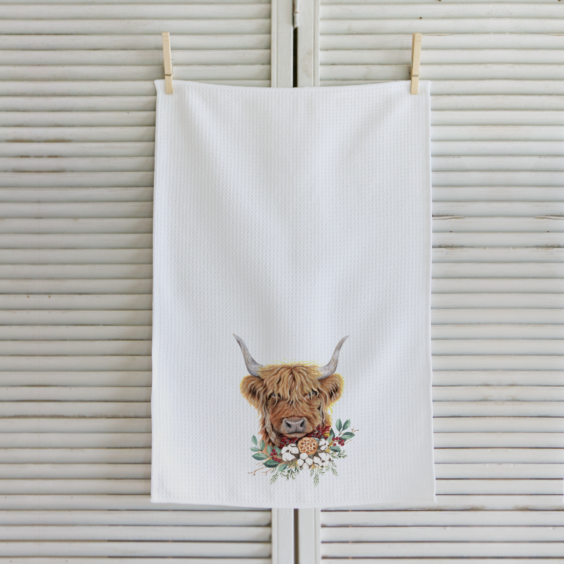 White towel with a highland cow design hanging on a wooden background
