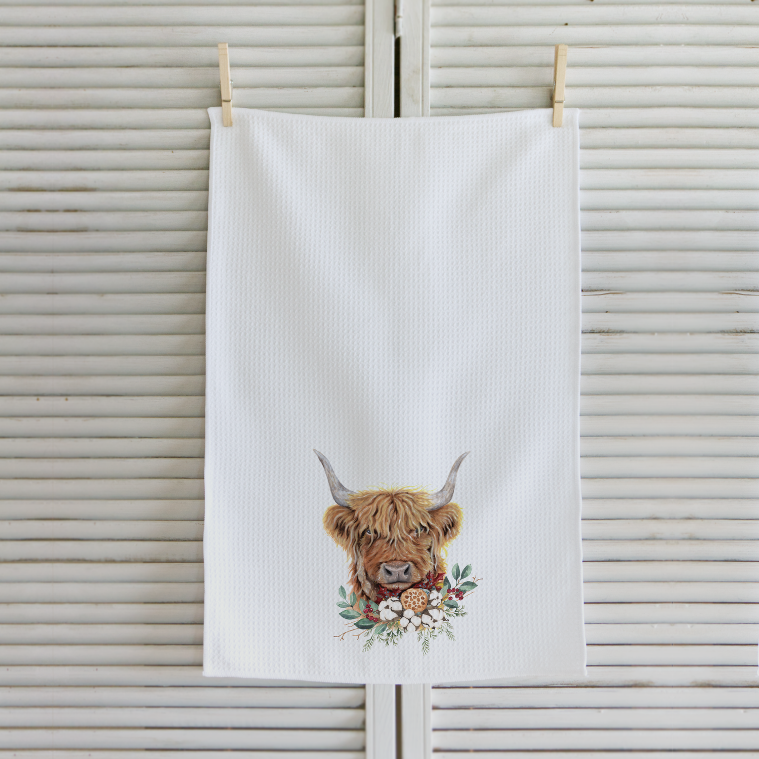 White towel with a highland cow design hanging on a wooden background