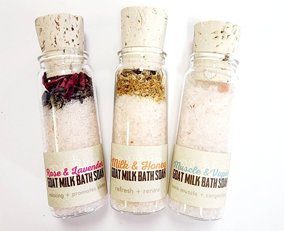 Three glass vials with cork lids, each filled with different bath soak blends. The vials are labeled with different scent combinations such as Milk & Honey and Rose & Lavender.