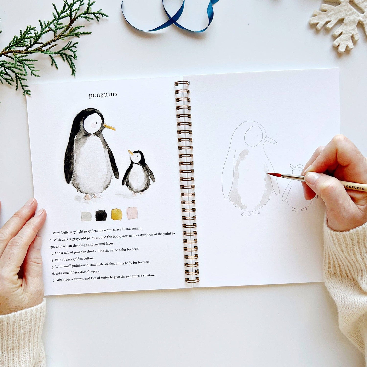 Person drawing penguins in a sketchbook with a coloring guide