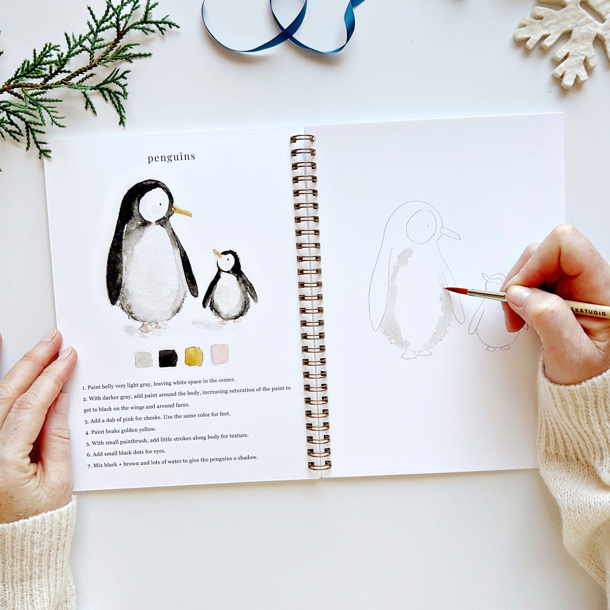 Person drawing penguins in a sketchbook with a coloring guide