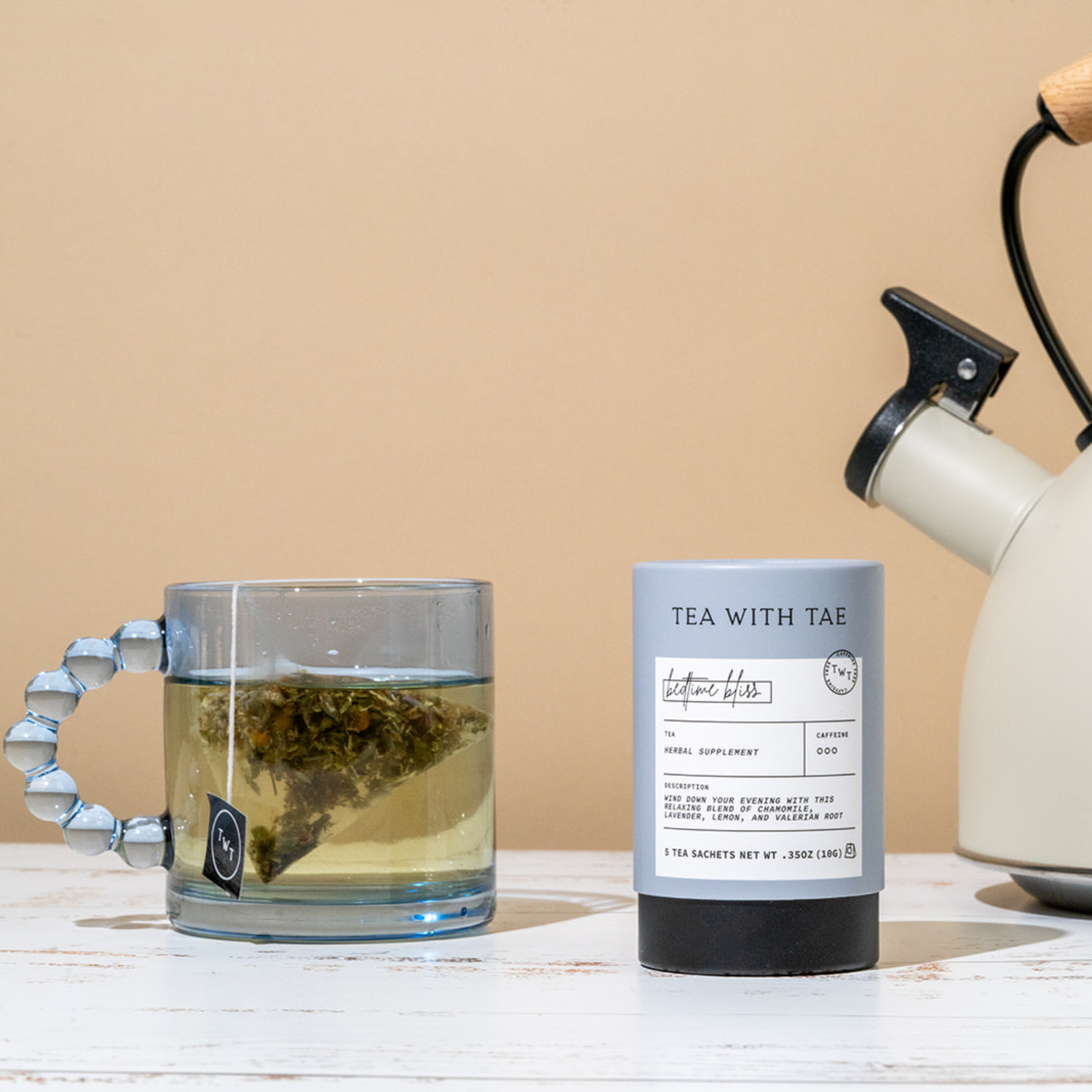 Tea with Tae package next to a glass mug with tea and a kettle on a wooden surface.