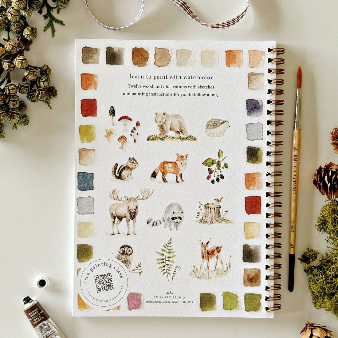 Notebook with nature-themed illustrations and color swatches on a white surface with decorative elements.