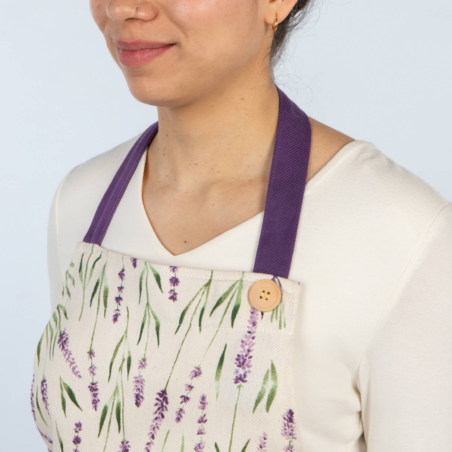 Person wearing a white apron with lavender design and purple straps on a light blue background
