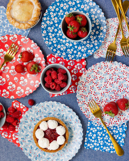 Dessert table with floral-patterned plates, bowls of berries, and pastries on a blue tablecloth.