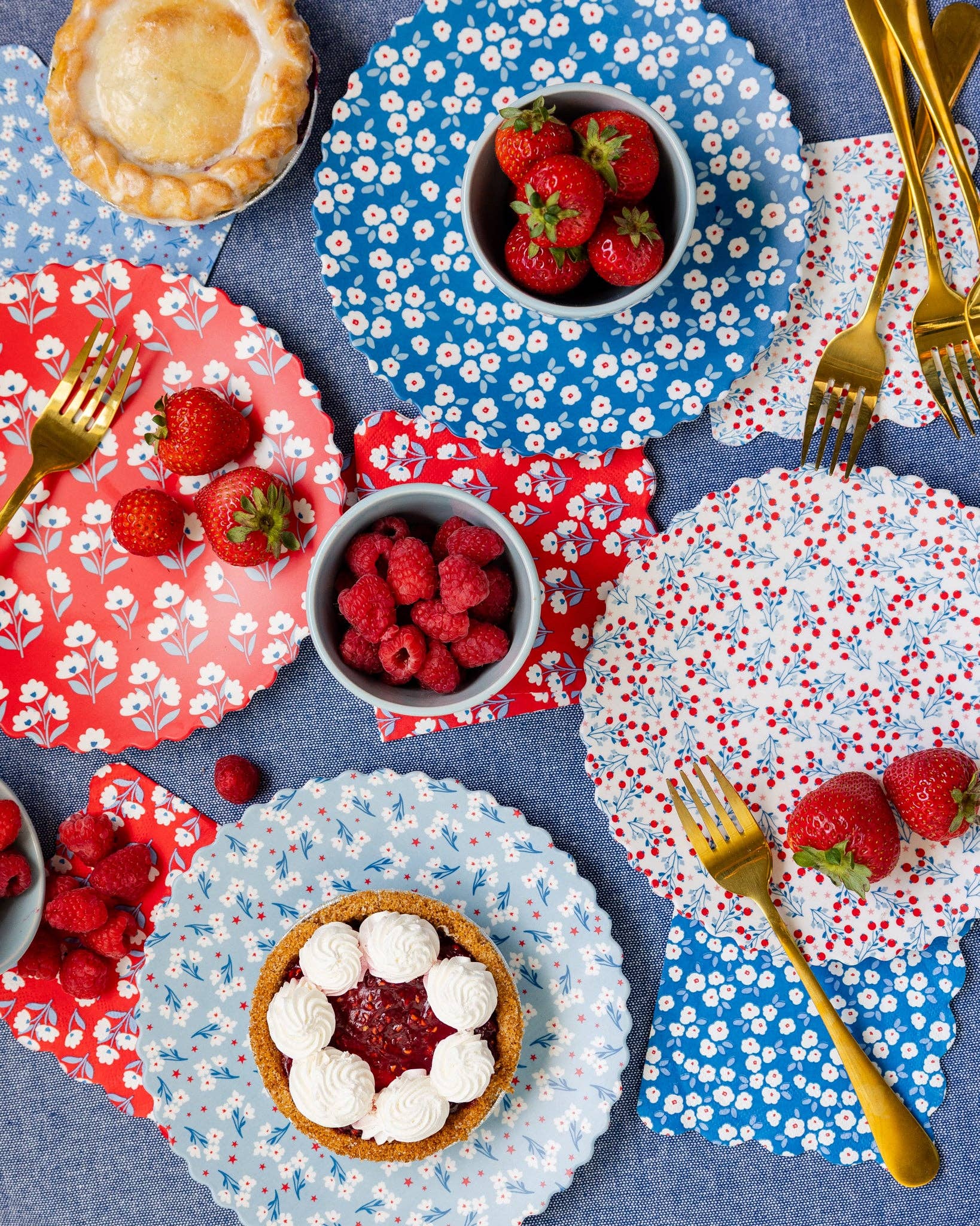 Dessert table with floral-patterned plates, bowls of berries, and pastries on a blue tablecloth.