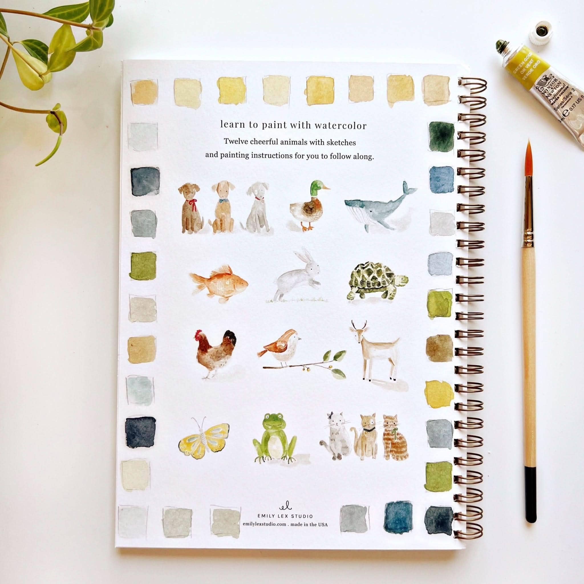 Artistic notebook with watercolor animals and color swatches on a white surface.