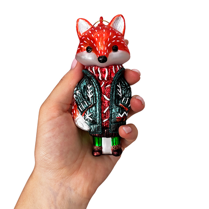 Hand holding a decorative fox ornament wearing a sweater on a white background