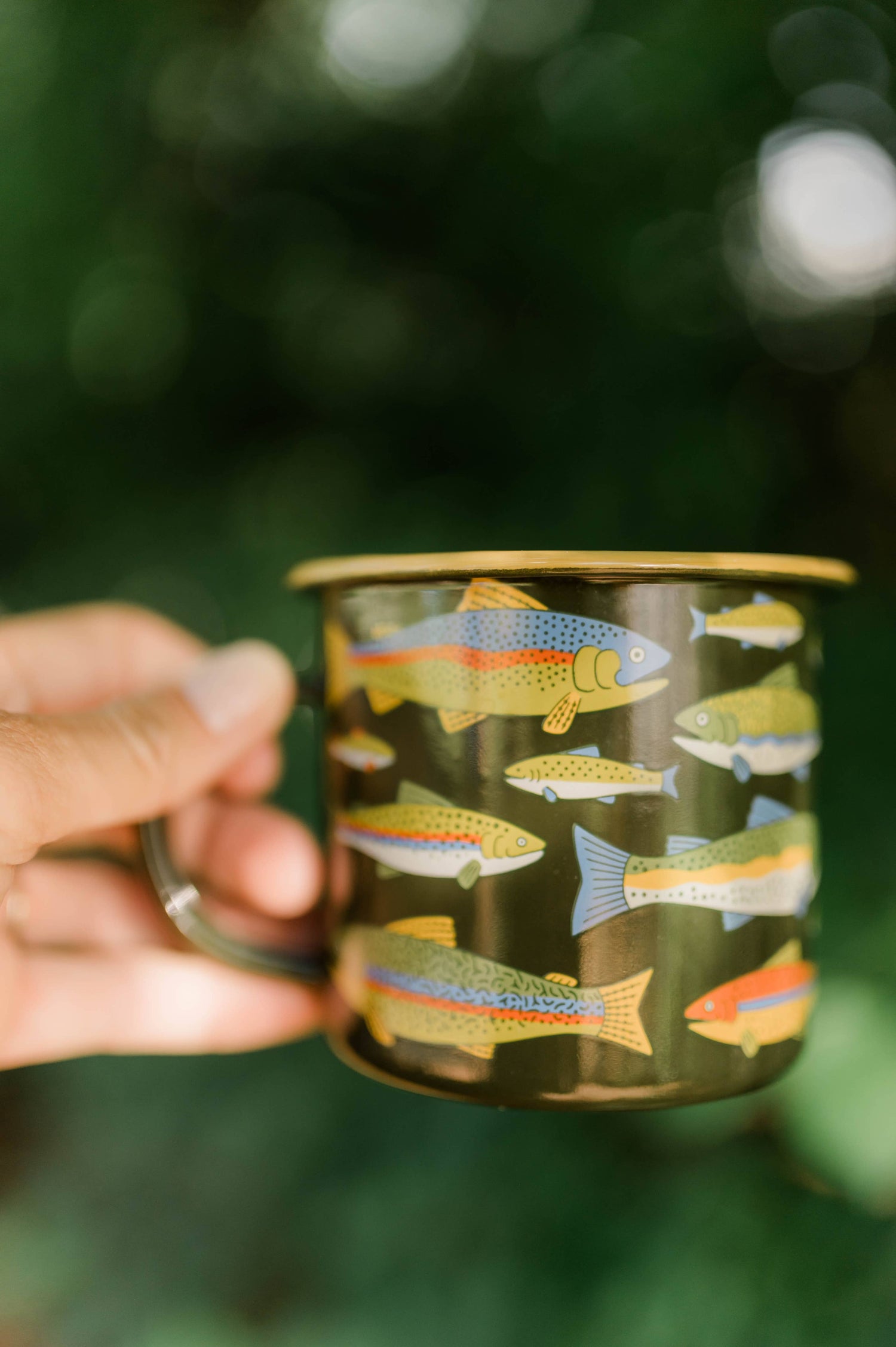 Hand holding a mug with fish design against a blurred green background