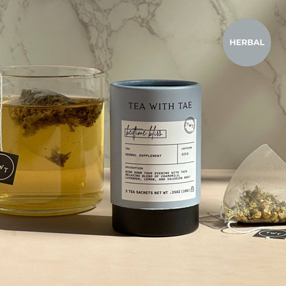 Tea with Tae herbal tea canister next to a glass of tea and a teabag on a marble surface.