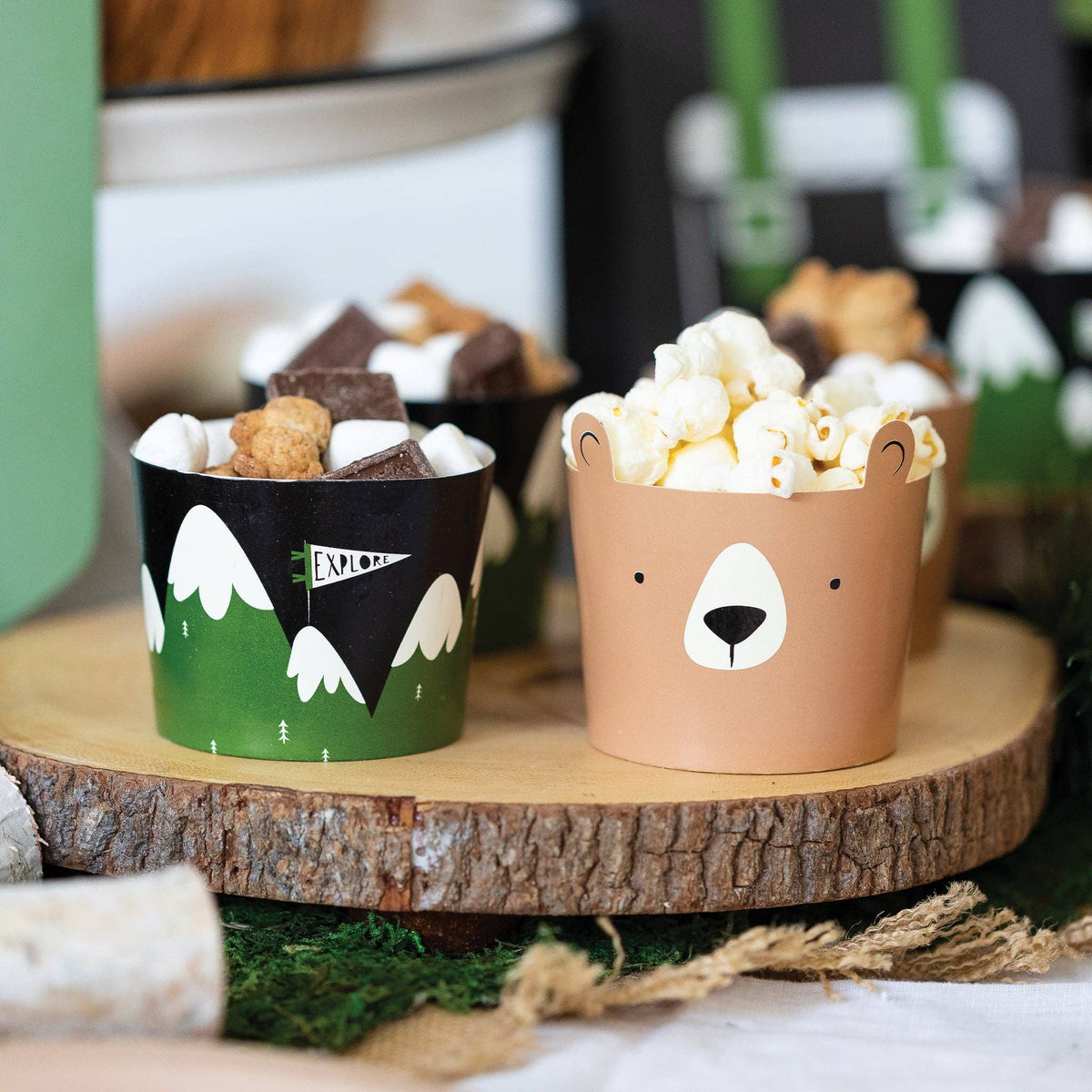 Two paper cups with animal designs filled with snacks on a wooden surface.