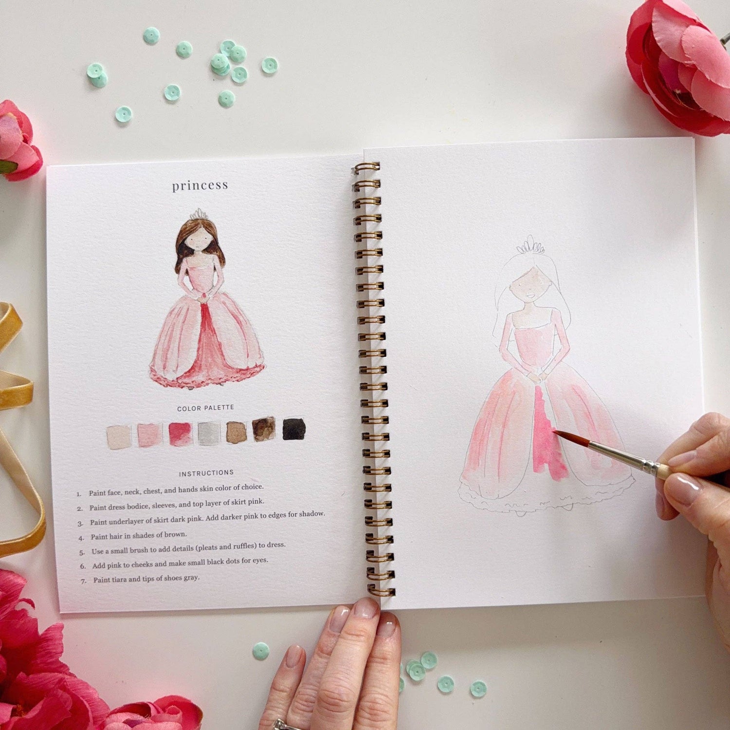 Open notebook with illustrations of a princess and color palette, surrounded by decorative elements.