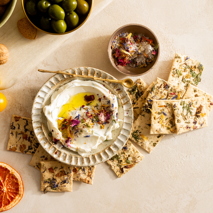 Dessert platter with a bowl of cream, crackers, and dried flowers on a light surface.