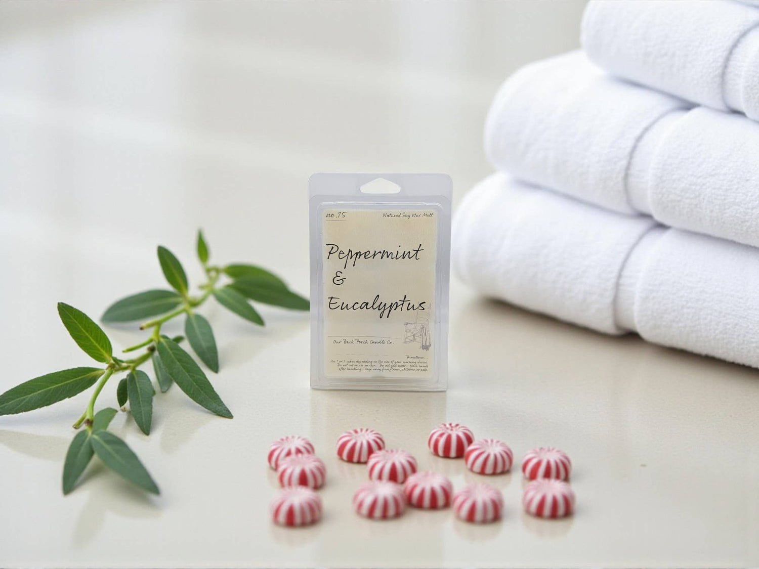 Wax tarts with peppermint and eucalyptus label next to a stack of white towels on a light surface.