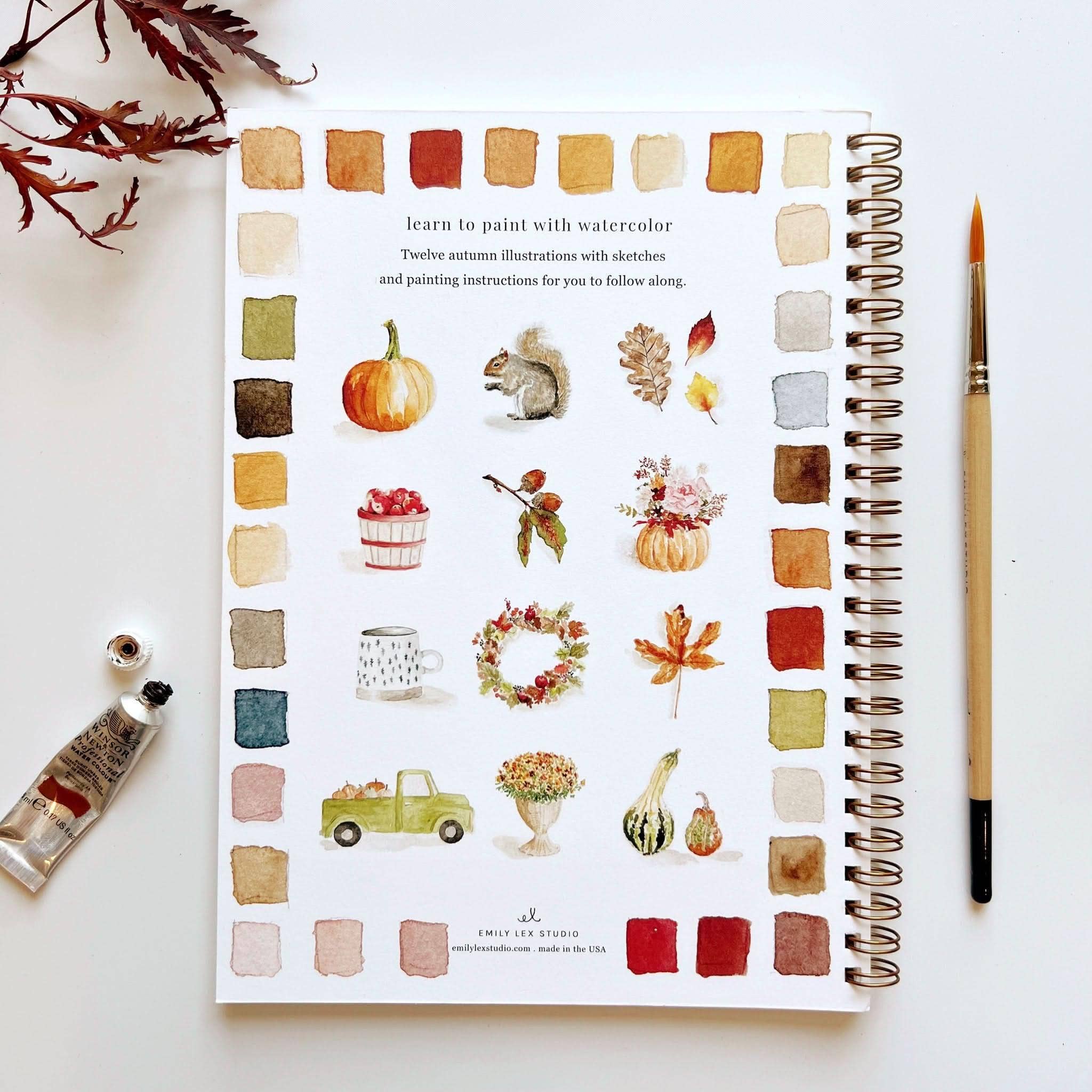 Watercolor painting guide with autumn illustrations and a brush on a white surface