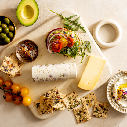 Platter with a sandwich, crackers, cheese, and a bottle of flower co product on a light background