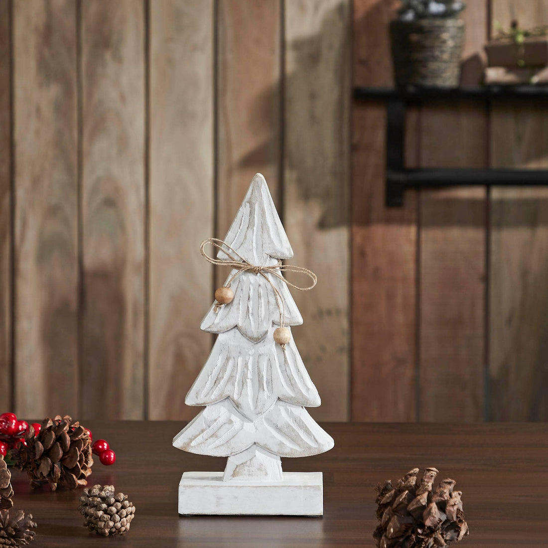 Decorative white Christmas tree figurine on a wooden surface with pine cones and berries.