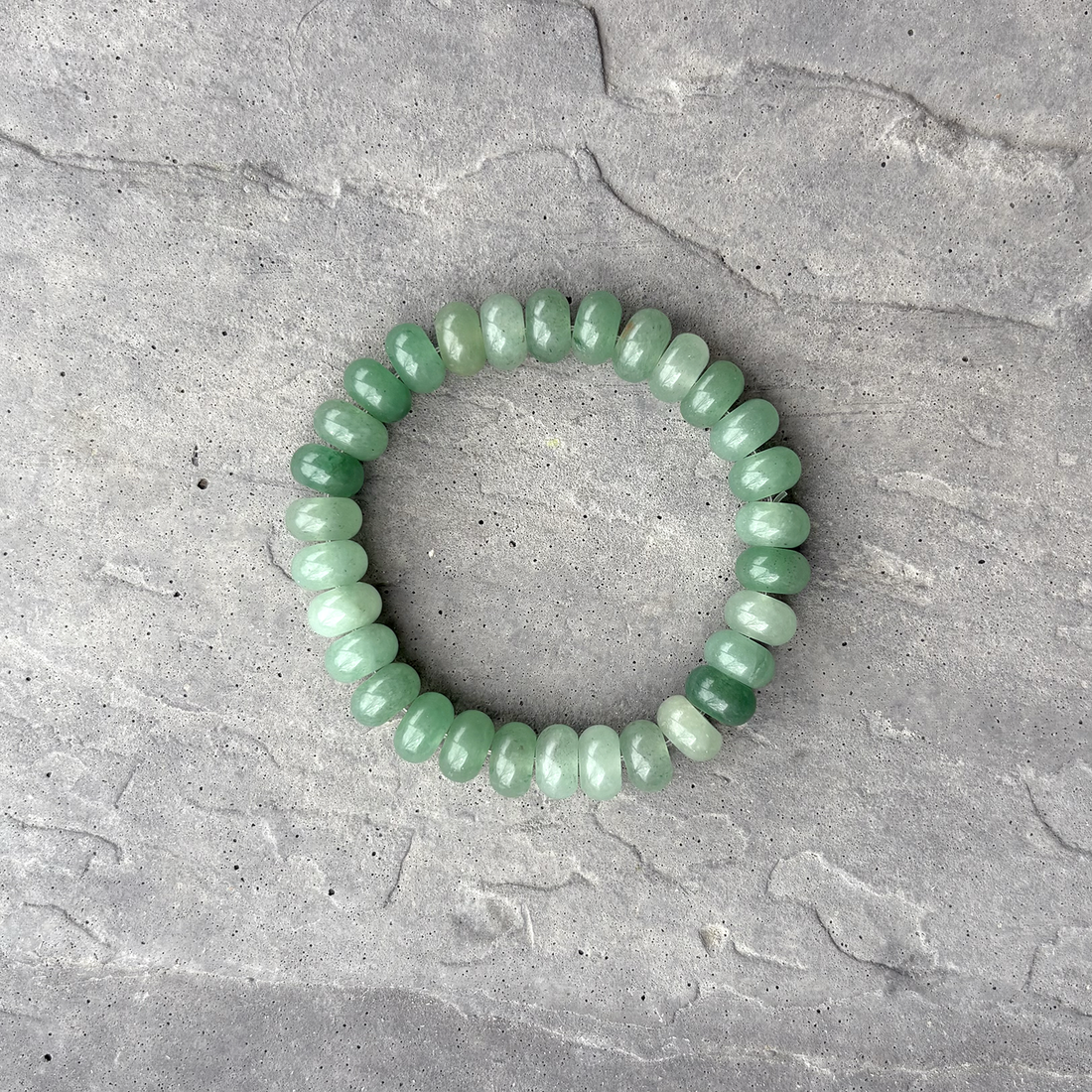 A stretchy bracelet with chunky 10mm Green Aventurine rondelle beads laid out on a grey surface.