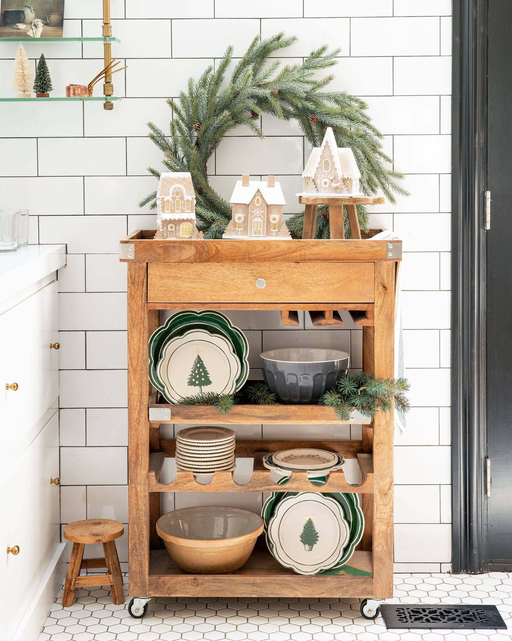 Wooden cart with decorative items in a kitchen setting with a wreath on the wall.