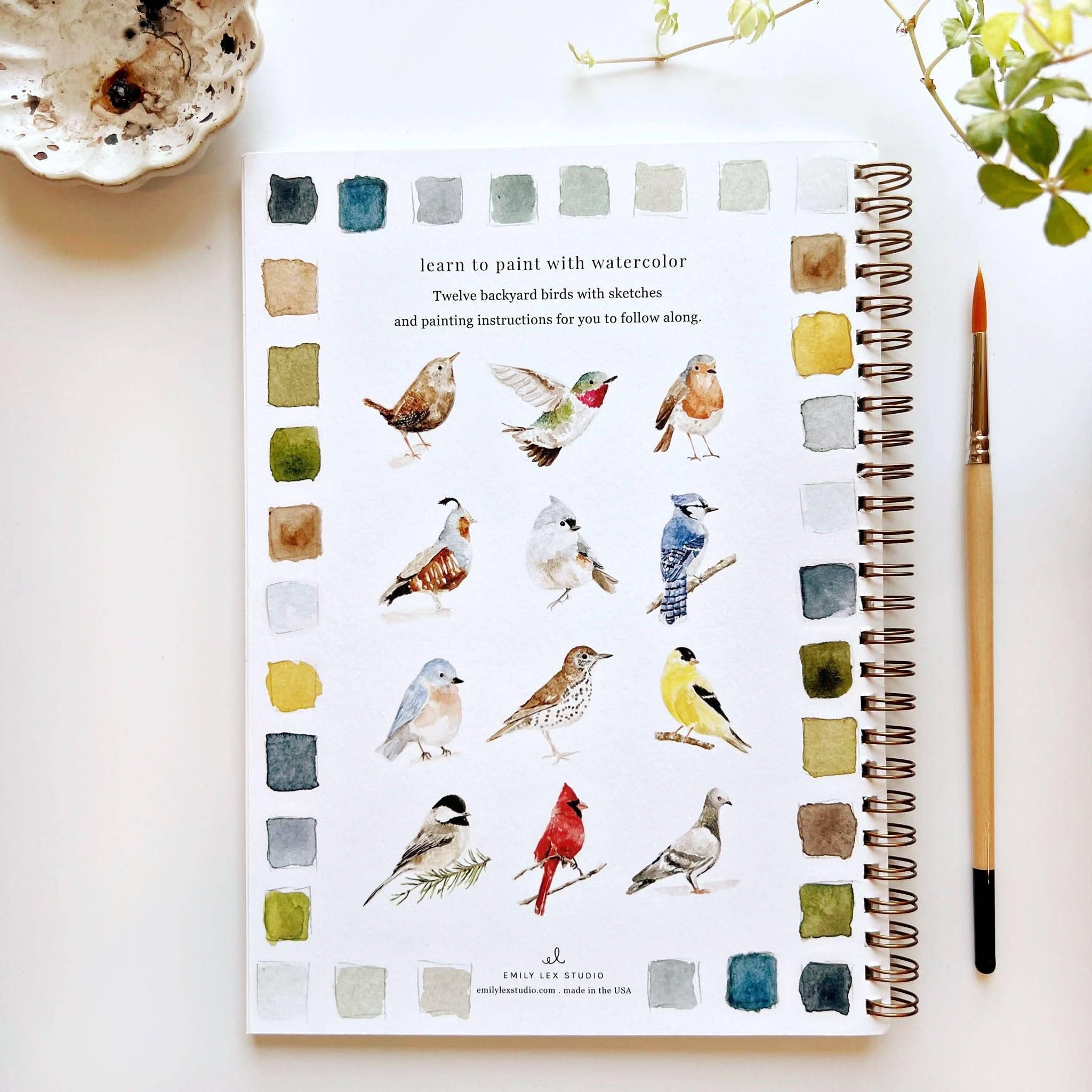 Notebook with watercolor illustrations of birds and a paintbrush on a white surface