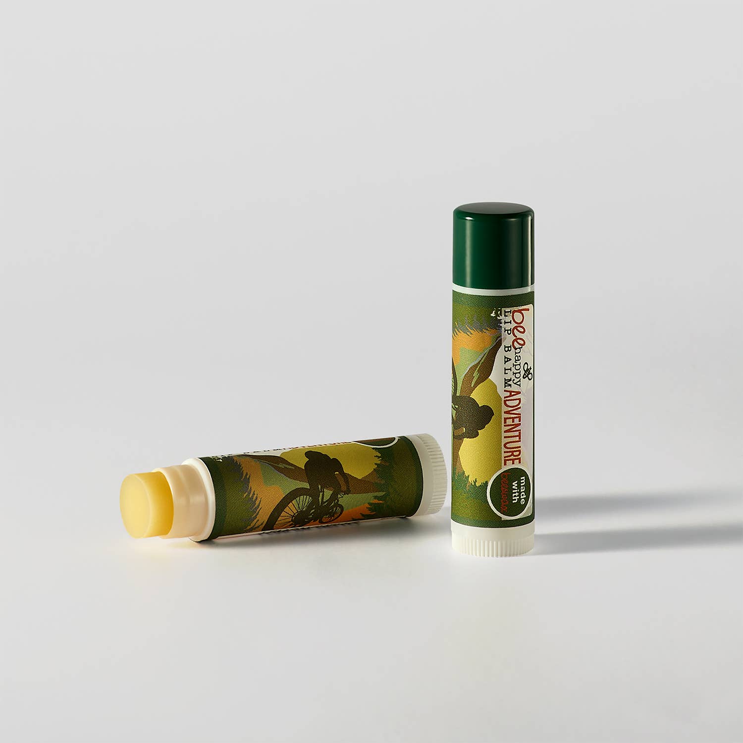Two lip balm tubes with nature-themed designs on a light gray background