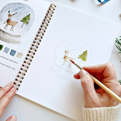 Person coloring a reindeer in a snow globe illustration in a notebook.