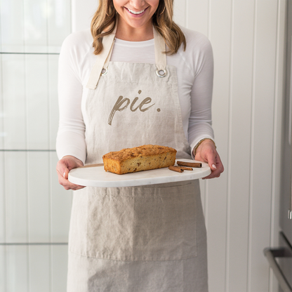 Person wearing a custom apron holding a loaf of bread in a kitchen.