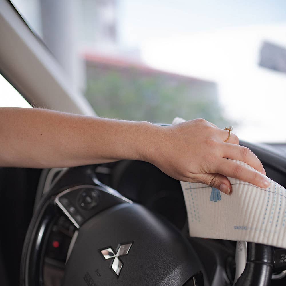 Person cleaning a car steering wheel and dashboard in the foreground
