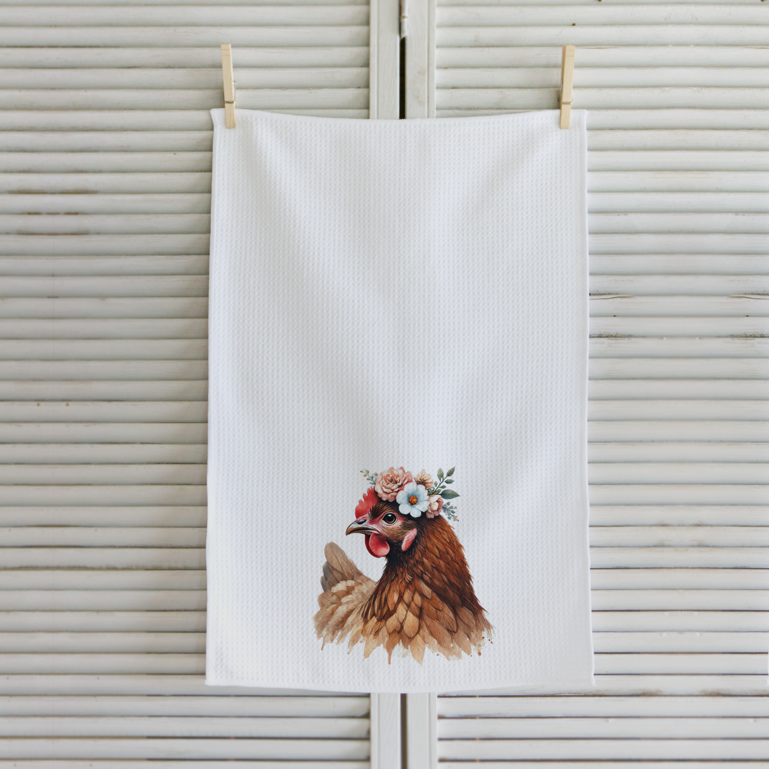 White towel with a chicken illustration wearing a flower crown hanging on a wooden surface.