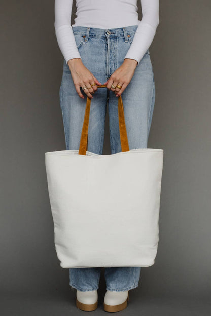 Person holding a white tote bag with brown handles against a gray background