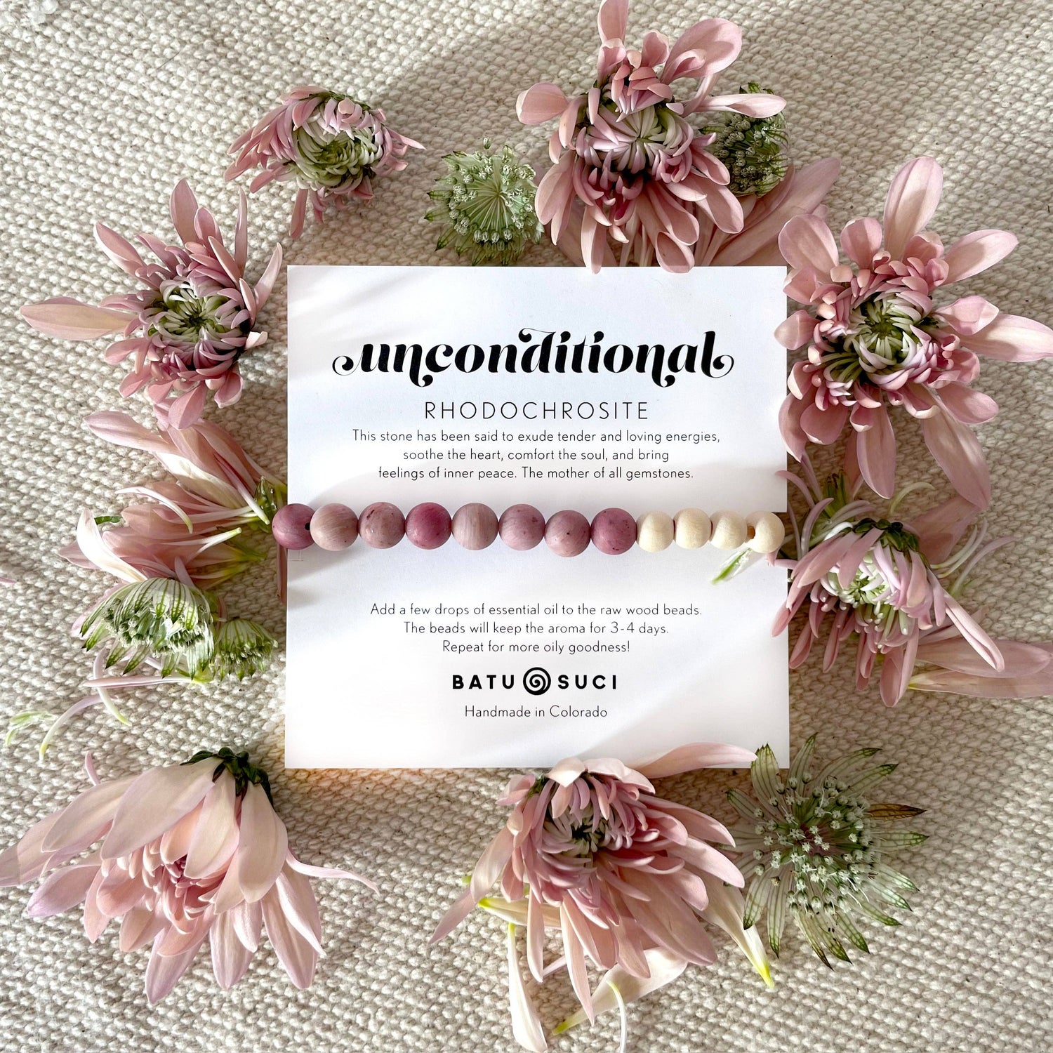 Beaded bracelet with card on a textured surface surrounded by pink flowers