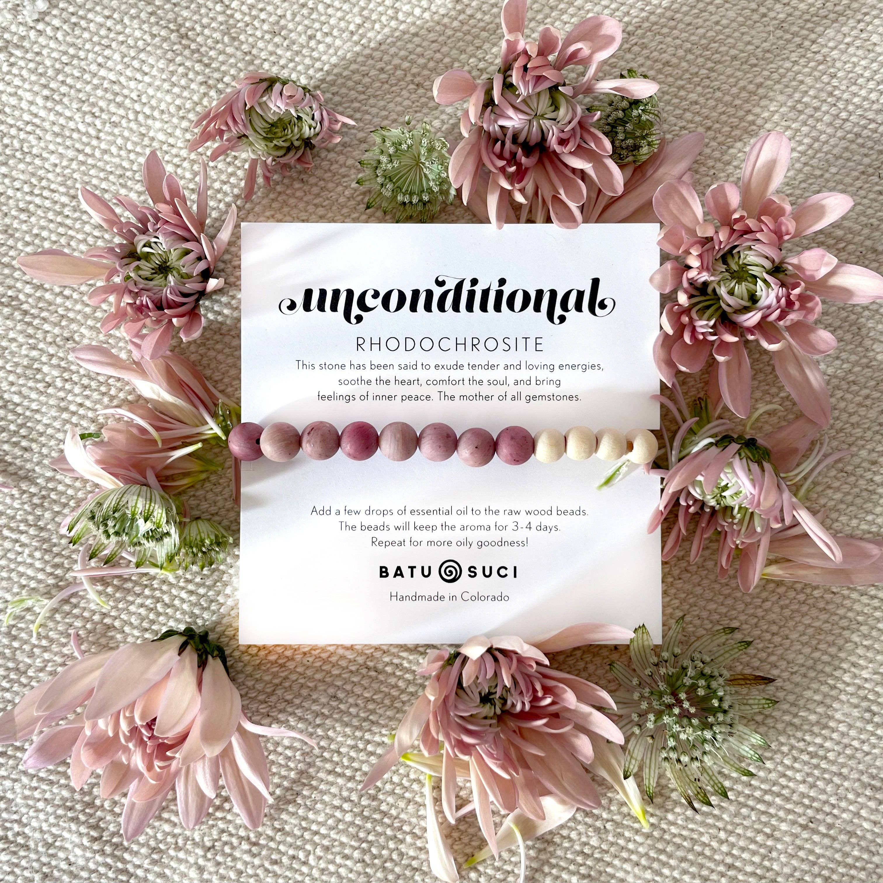 Beaded bracelet with card on a textured surface surrounded by pink flowers
